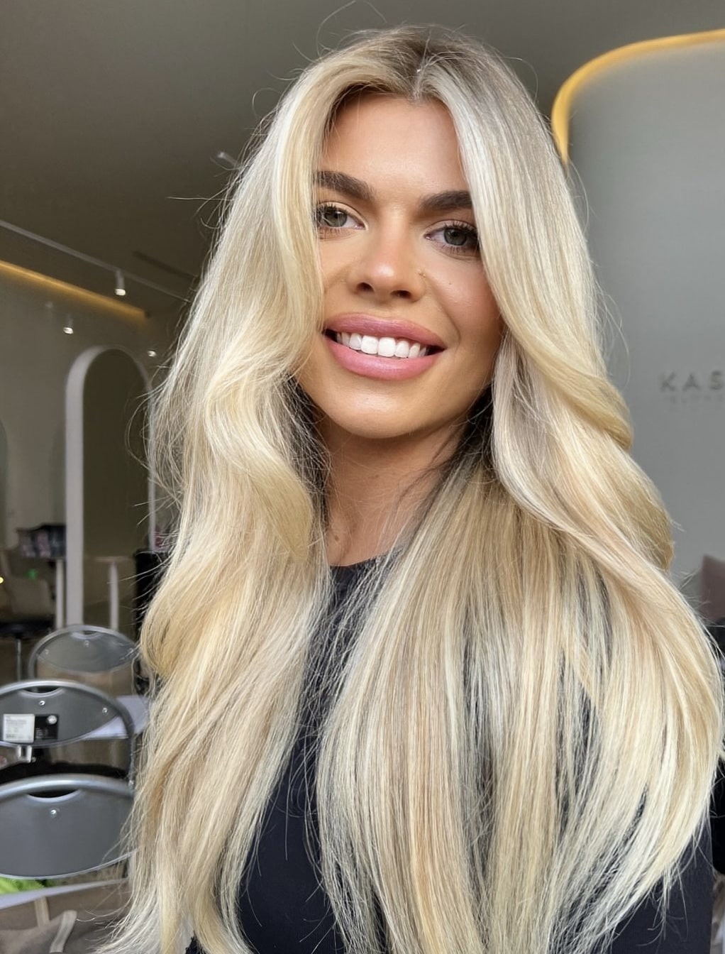 Smiling woman with long wavy blonde hair, showing off her low maintenance blonde style.